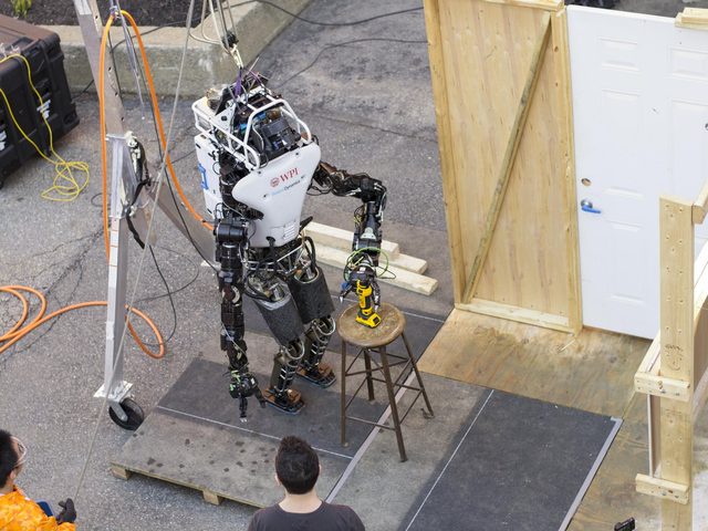 Overhead view of Atlas reaching for the drill on a stool